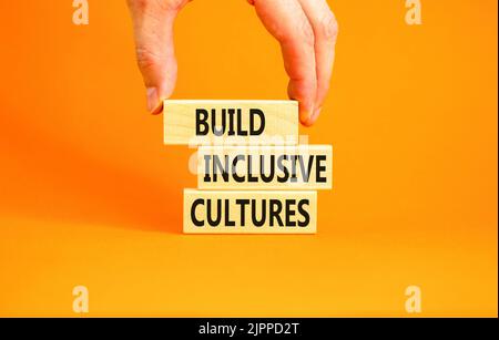 Build inclusive cultures symbol. Concept words Build inclusive cultures on wooden blocks. Businessman hand. Beautiful orange background. Business buil Stock Photo