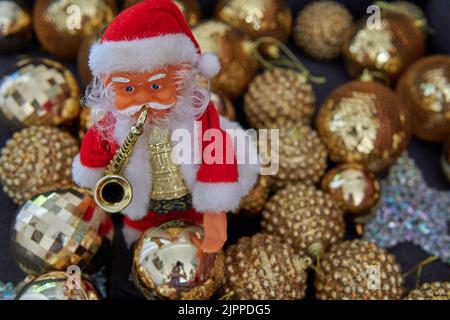 little doll of Santa Claus with saxophone on front with golden Shimmering balls in background. Christmas decoration Stock Photo