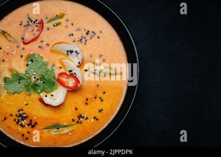 Thai soup in a plate with chicken on black stone on gray concrete Stock Photo