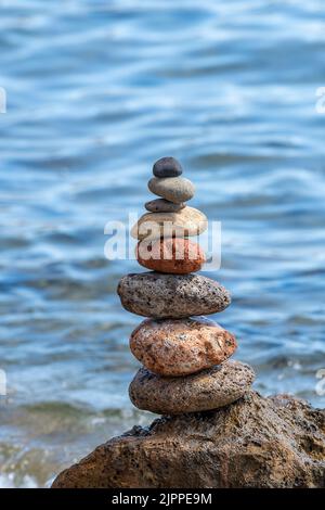 rocks balancing on each other forming a tower or stones balanced on one another to make a tall pile or tower on the beach at the seaside in greece. Stock Photo