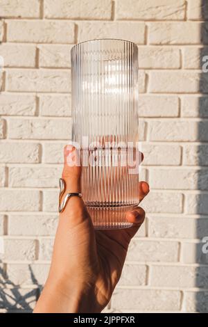 Close-up of woman's hand holding a crystal glass with clean water in natural sunlight over the white brick wall Stock Photo