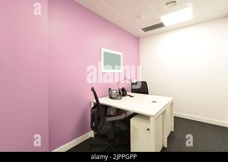 Small office cubicle with a double white desk, matching chest of drawers, black swivel chairs and switchboard phones Stock Photo