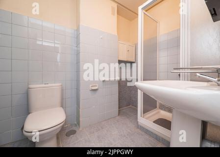 Simple restroom with white tiled shower stall, sliding doors, white toilets and blue tiles Stock Photo