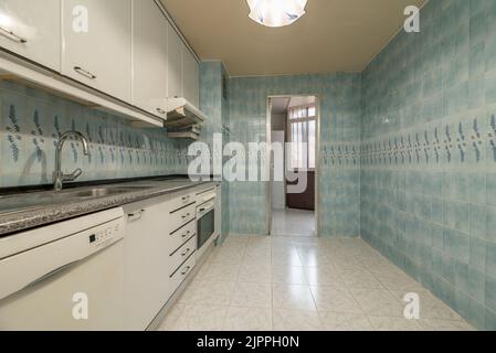 Kitchen with white wooden cabinets, built-in appliances, pink granite countertops and blue tiles on the walls Stock Photo