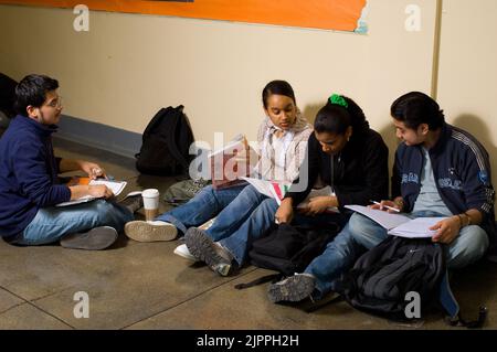 Public School High School male and female students sitting in corridor between classes looking at schoolwork and talking to each other Stock Photo
