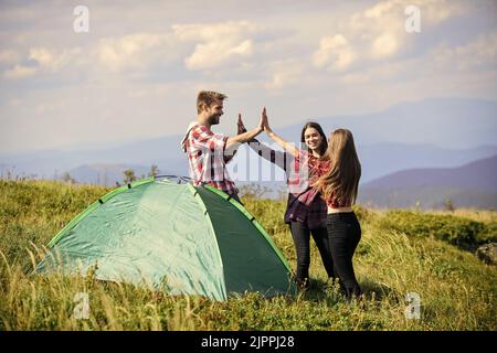 Well done. Camping gear. Camping tent. Good job. Teamwork concept. Hiking activity. Friends set up tent on top mountain. Camping equipment. Weekend in Stock Photo