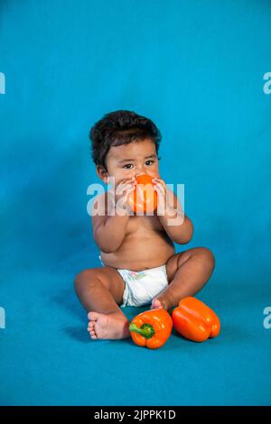 Healthy Native American baby, from the Santa Clara Pueblo in New Mexico plays with  three large orange bell peppers Stock Photo