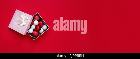 Banner made from Christmas decorations in pink open gift box on red background. Red and white round toys. Concept of Christmas and New Year or romantic Valentines Day. Copy space for text. Stock Photo