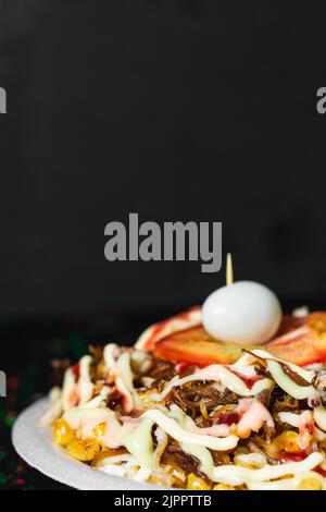 detail shot of a typical colombian street food dish, arepa with chicken and shredded beef with corn, sauces, tomato and quail egg, on a table decorate Stock Photo