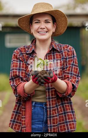 Sustainable farmer holding a plant or seedling outdoors smiling and happy about her organic farm or garden. Young female nature activist that is Stock Photo