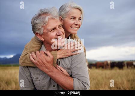 Mature couple embracing and looking happy while bonding outdoors at a farm, carefree and loving. Senior husband and wife having peaceful day in nature Stock Photo