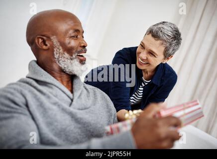 Happy anniversary my love. an attractive senior woman surprising her husband with a gift at home. Stock Photo