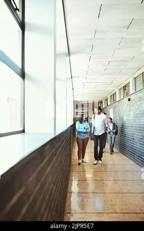 Arriving on campus for their first class. Full length shot of a group of university students walking through a campus corridor. Stock Photo