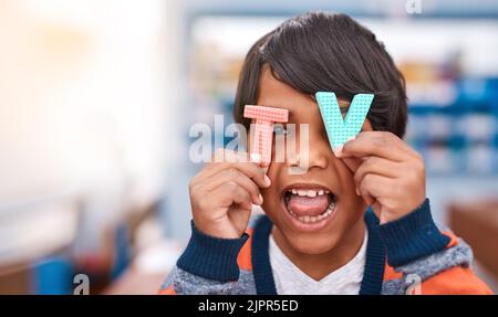 Mom always says I watch too much TV. a cheerful elementary school kid holding the letters T and V in front of his eyes inside of the classroom. Stock Photo