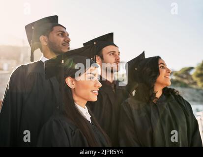 This accomplishment has inspired greatness in them all. a group of students standing together on graduation day. Stock Photo