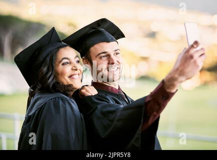 Look who made it to the top. two students taking a selfie together on graduation day. Stock Photo