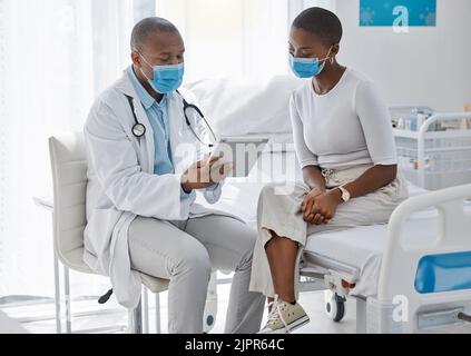 A doctor consulting a patient and talking to her about the covid virus using a tablet at the hospital or clinic. Female at her appointment or Stock Photo