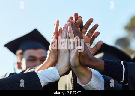 Our years of hard work has paid off. Closeup shot of a group of unrecognisable students high fiving on graduation day. Stock Photo