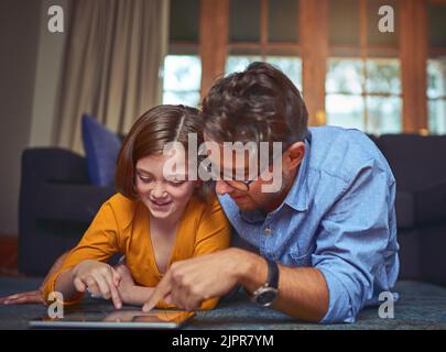 Learning about online safety. a father and daughter lying on the floor and using a digital tablet together at home. Stock Photo
