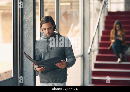 Hes a diligent student. a handsome young university student studying while standing in a hallway on campus. Stock Photo