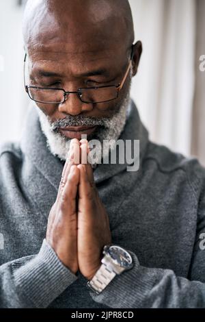 Seeking guidance from above. a handsome senior man praying while sitting in his home. Stock Photo