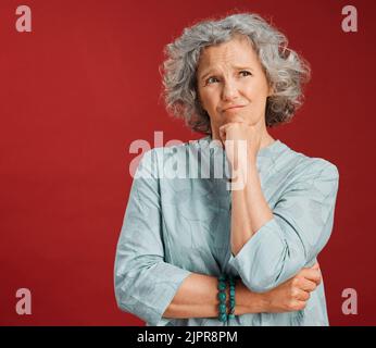 Thinking, confused and wondering woman looking puzzled, unsure and uncertain about choice, decision and idea in mind against studio red background Stock Photo
