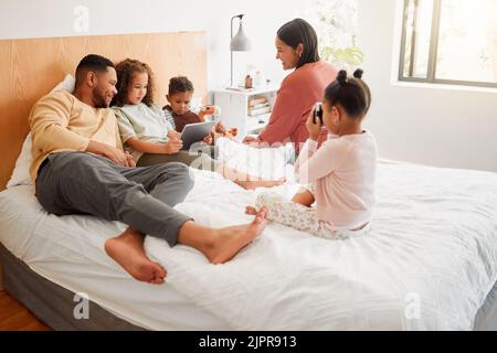 Happy family in the bedroom as the mother and father play, smile and relax with their children. Brother and sisters sitting together with their mom Stock Photo