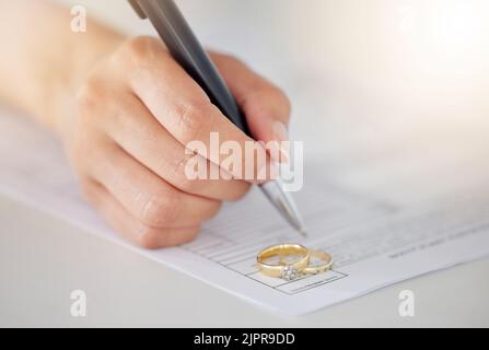 .Woman hand signing legal divorce documents, deal or paper contract in a lawyer office with ring placed on table. Person writing signature on marriage Stock Photo