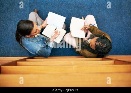 Working together to stay on top of their studies. High angle shot of two university students working together in the library at campus. Stock Photo