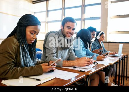 Campus communication. Cropped portrait of a handsome young university student sitting in class with other students. Stock Photo