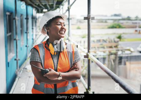 A happy, smiling and cheerful young black woman or senior construction industry worker standing at a building site. A professional female employee Stock Photo