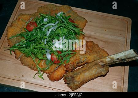 Veal Milanese, or veal alla Milanese, is an Italian popular dish,traditionally prepared with a veal rib chop or sirloin bone-in and made into a breade Stock Photo