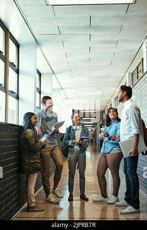 Casual conversations on campus. Full length shot of a group of university students talking while standing in a campus corridor. Stock Photo
