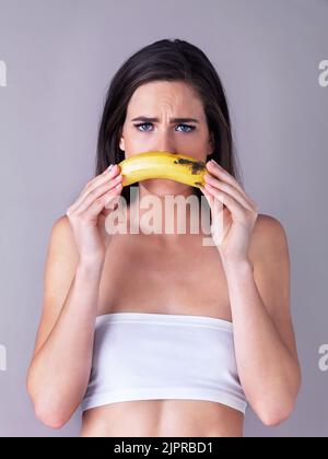 Shes one sad monkey...Studio portrait of an attractive young woman holding a banana against a purple background. Stock Photo