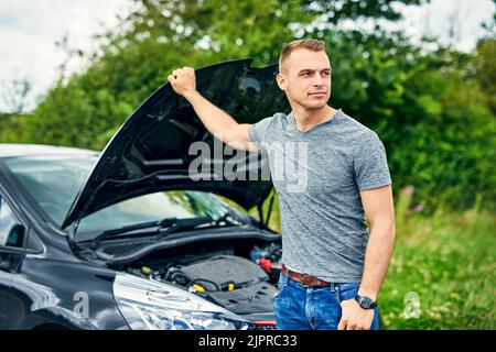 Hes in desperate need of some roadside assistance. a young man checking under the hood of his car after breaking down on the road. Stock Photo