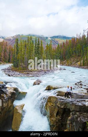 Sunwapta Falls Jasper National Park, Canada. The Canadian Rockies during the Autumn fall season. A couple of men and women visiting Sunwapta falls standing on the edge of the rocks by the river Stock Photo