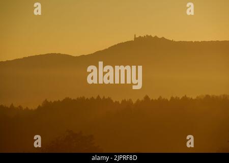 Pastel colored landscape shot at sunrise in autumn. Trees in front of a mountain with castle. Different layers of different color tones. Germany, Teck Stock Photo