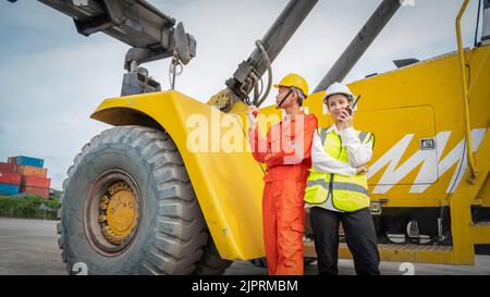 Woman Manager and foreman using walkie talkie at side of Cargo forklift in warehouse , Manager use tablet in white helmet Safety Supervisor in Contain Stock Photo