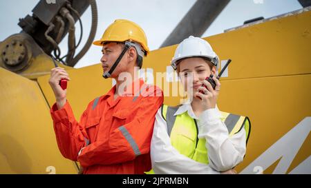 Woman Manager and foreman using walkie talkie at side of Cargo forklift in warehouse , Manager use tablet in white helmet Safety Supervisor in Contain Stock Photo
