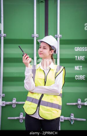 Female Foreman stay in front of container cargo using walkie talkie for communication and control forklift concept service transportation logistic. Sa Stock Photo