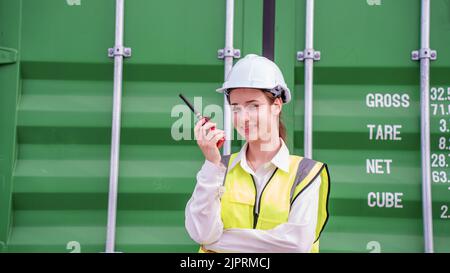 Female Foreman stay in front of container cargo using walkie talkie for communication and control forklift concept service transportation logistic. Sa Stock Photo