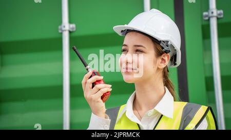 Female Foreman stay in front of container cargo using walkie talkie for communication and control forklift concept service transportation logistic. Sa Stock Photo