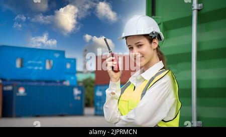 Female Foreman stay in front of container cargo using walkie talkie for communication and control forklift concept service transportation logistic. Sa Stock Photo