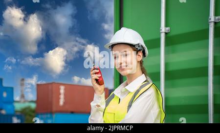 Female Foreman stay in front of container cargo using walkie talkie for communication and control forklift concept service transportation logistic. Sa Stock Photo