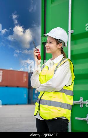 Female Foreman stay in front of container cargo using walkie talkie for communication and control forklift concept service transportation logistic. Sa Stock Photo