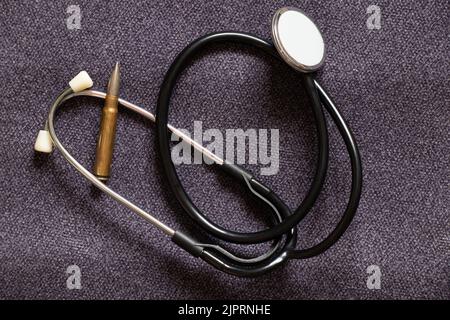 Stethoscope of a doctor and a bullet of a soldier ledat on a gray background, military medicine during the war in Ukraine, health hazard Stock Photo