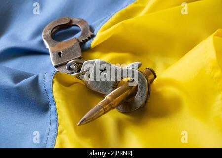 Handcuffs and a bullet lie on the yellow-blue flag of Ukraine, laws in Ukraine, democracy and war in Ukraine, home defense Stock Photo