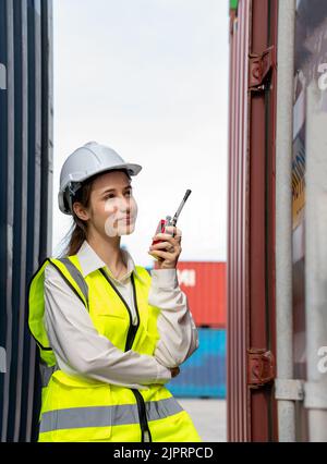 Woman foreman smile using walkie talkie in front of Cargo forklift in warehouse , Manager in white helmet Safety Supervisor in Container Custom Termin Stock Photo