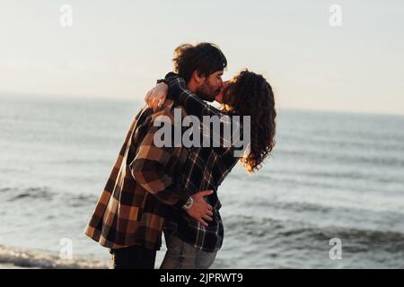 Woman and man hugging and kissing with sea on the background, young couple fall in love Stock Photo