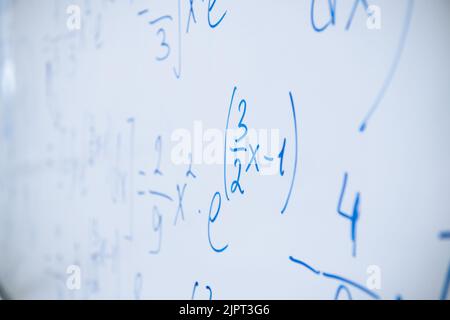 Physical and mathematical formulas written with a blue marker on a white board in a high school classroom. Abstract background close-up. Stock Photo